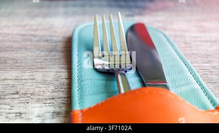 Gabel und Messer ruhen in einem farbenfrohen Lederetui auf einer Holzoberfläche im weichen Licht Stockfoto