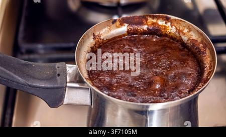 Frischer Kaffee, der in einer Kupfer-Cezve auf dem Herd mit authentischem Zubereitungsprozess köchelt Stockfoto