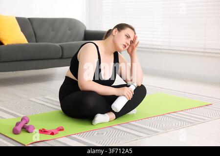 Müde übergewichtige Frau auf Fitnessmatte zu Hause, Platz für Text Stockfoto
