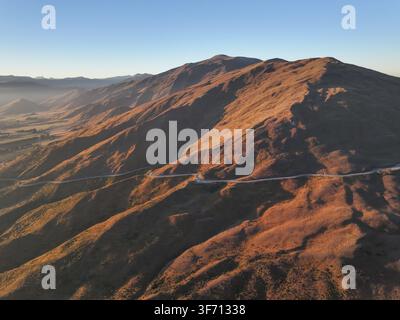 Luftbild des Crown Range Road Scenic Lookout, der sich während der goldenen Stunde durch die rauen Berge der Region Otago windet, Roaring Meg, Region Otago Stockfoto