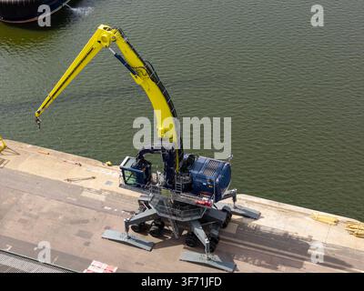 Luftaufnahme einer großen gelben und blauen mobilen Hafenkräne, die auf einem Betondock neben einem ruhigen Gewässer in Großbritannien positioniert ist. Stockfoto