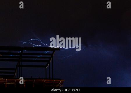 Ein heller Blitz zuckt über einen dunklen Nachthimmel über dem Stahlgerüst eines im Bau befindlichen Gebäudes. Stockfoto