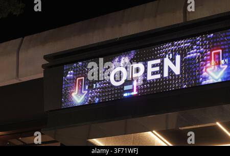 Digitale LED-Werbetafel zeigt ein leuchtendes „Offen“-Schild mit lebendigen Neonpfeilen und abstrakten digitalen Mustern, das die Geschäftseröffnung und den Modus anzeigt Stockfoto