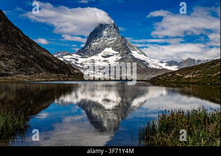 Der schneebedeckte Gipfel des Matterhorns spiegelt sich in den stillen Gewässern des Riffelsees unter einem teilweise bewölkten Himmel wider. Stockfoto