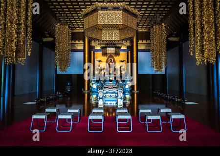 Ein aufwendiger goldener Zeremonienaltar mit hängenden Laternen und einer sitzenden Buddhastatue füllt das dunkle Holzinnere der Haupthalle des Zojoji-Tempels. Stockfoto