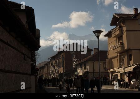 Fußgänger genießen einen frischen Tag in Bansko, Bulgarien, bei einem Spaziergang durch die traditionelle Architektur mit den majestätischen Pirinbergen darüber. Stockfoto