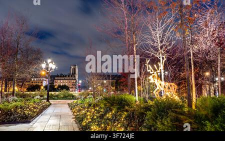 Beleuchteter Stadtpark mit Weihnachtslichtern und einer Hirschskulptur bei Nacht mit der Kathedrale Notre-Dame in Paris, Frankreich. Stockfoto