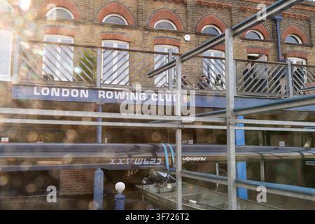 Mitglieder entspannen sich auf dem Balkon des historischen Londoner Ruderclubs am Putney Embankment, London, umgeben von Ruderbooten, die für das Training gelagert sind. Stockfoto