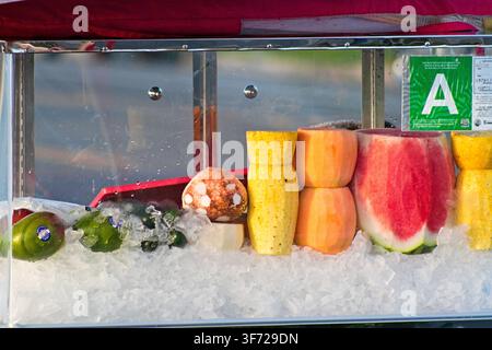 Frische Früchte liegen auf zerkleinertem Eis in einem klaren Glasbehälter. Wassermelonen-, Melonen- und Kiwistücke sind ordentlich angeordnet. Ein grüner Aufkleber kennzeichnet die Qualitätsklasse 'A'. Stockfoto