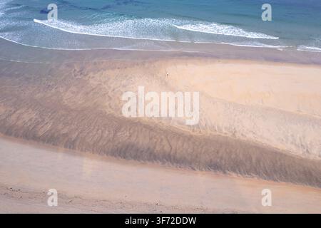Atemberaubender Luft-Drohnenbild eines breiten Sandstrands mit blauen Meereswellen, die am Ufer brechen Stockfoto