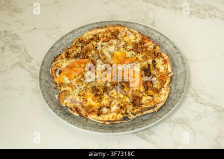Kapsalonpizza mit gegrilltem Fleisch, Tomatenscheiben und roten Zwiebeln auf einem gesprenkelten Teller Stockfoto