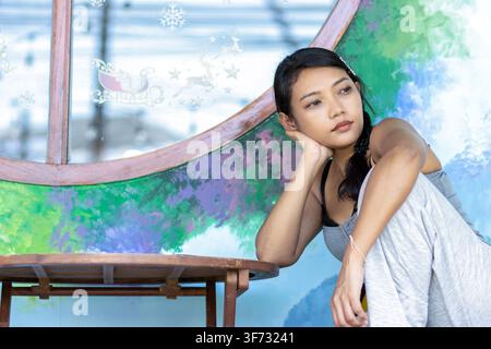 Nachdenkliche junge asiatische Frau sitzt nachdenklich an einem Holztisch Stockfoto