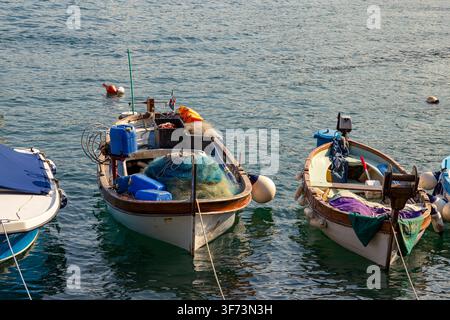Kleine Fischerboote treiben auf ruhigem Adriawasser in Lovran, Kroatien. Netze, Seile, Behälter und Bojen ruhen auf den Decks nahe dem Hafen. Stockfoto