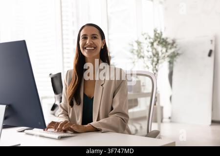 Glückliche Geschäftsfrau sitzt am Schreibtisch und arbeitet am Computer Stockfoto