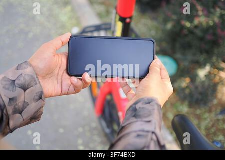 Person, die ein Smartphone hält, um den QR-Code eines Fahrrads zur Miete auf der Straße zu scannen Stockfoto