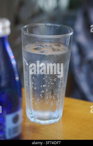 Ein Glas Sprudelwasser oder kohlensäurehaltiges Getränk, serviert mit Eisbläschen, die in einem facettierten Tumbler auf einem Holztisch sichtbar sind Stockfoto