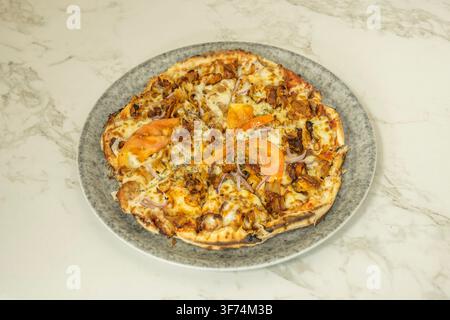 Kapsalonpizza mit gegrilltem Fleisch, Tomatenscheiben und roten Zwiebeln auf einem gesprenkelten Teller Stockfoto