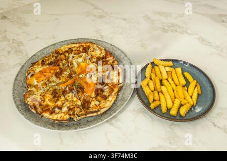 Kapsalon Pizza mit Tomaten, Zwiebeln und Beilage Crinkle-Cut-Pommes auf Marmor Stockfoto