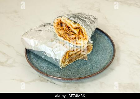 In Folie gewickelte türkische Pizzarolle aufgeschnitten, zeigt die geschichtete Füllung auf blauem Teller Stockfoto