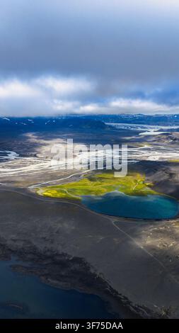 Luftbild-Drohnenperspektive der isländischen Hochlande mit geflochtenen Gletscherflüssen, türkisfarbenem Geothermalsee, schwarzem Vulkansand und Grün Stockfoto