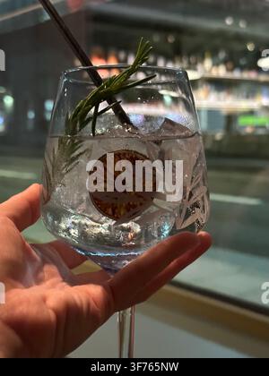 Erfrischender Cocktail mit Rosmarin und getrockneter Zitronenscheibe in der Hand. Kühliges alkoholisches Getränk mit Eiswürfeln und aromatischen Kräutern in einem Glas. Perfekte Wahl fo Stockfoto
