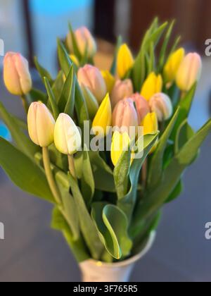 Wunderschönes Bouquet aus frischen rosa und gelben Tulpen in einer Vase. Ein bezauberndes Arrangement von Frühlingsblumen mit pastellfarbenen Blüten und üppigem Grün Stockfoto