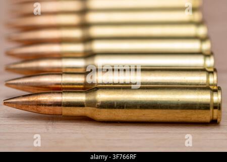 Eine Nahaufnahme zeigt mehrere Messingpatronen, die in einer horizontalen Reihe auf einer Holzoberfläche angeordnet sind. Stockfoto