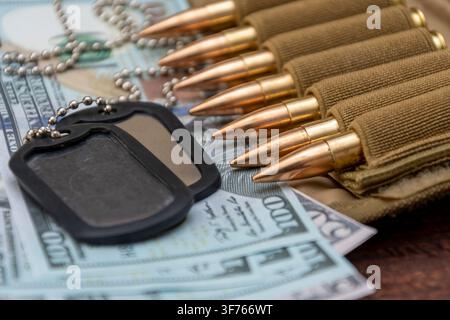 Nahaufnahme von Militärhundeausweisen und Gewehrpatronen auf verstreuten Hundert-Dollar-Scheinen. Stockfoto