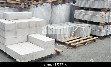 Frontansicht von gestapelten grauen Schotterblöcken (Schlackenblöcken) und verpackten Baumaterialien auf Holzpaletten, ideal für Mauerwerk, Wandbau und Stockfoto