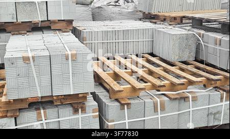 Nahaufnahme von gebündelten Betonpflasterplatten, die mit Umreifungsbändern auf Holzpaletten gesichert sind, ideal für Bauversorgungsvisuals, Materialinventar Stockfoto