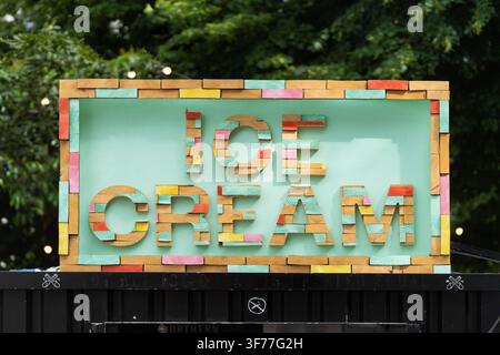 Ein lebendiges Schild mit der Aufschrift "ICE CREAM" aus Holzblöcken markiert einen Verkäuferstand auf der South Bank in London und zieht Besucher mit einer farbenfrohen Auslage an. Stockfoto