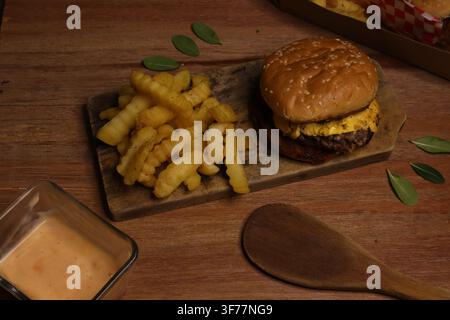 Saftiger Rindfleisch-Burger mit Pommes und Sauce, serviert auf Holzbrett Stockfoto