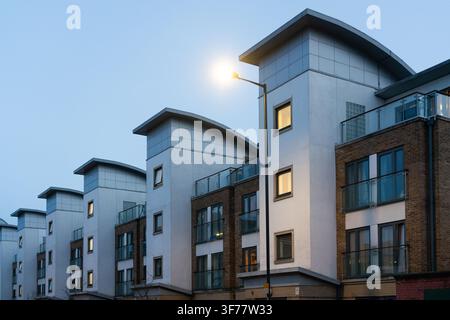 Die modernen Wohnapartments im Greenwich Millennium Village, London, sind in der Dämmerung beleuchtet und werfen ein warmes Licht auf ihr einzigartiges Design. Stockfoto