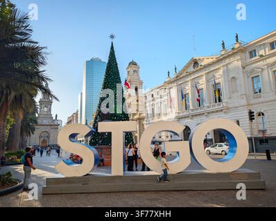 SANTIAGO, CHILE - 03. DEZEMBER 2025: Ein großes STGO-Schild steht in der Nähe eines hohen Weihnachtsbaums auf der Plaza de Armas mit historischen Gebäuden in der Nähe in Santiago, Chil Stockfoto