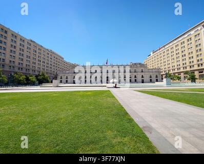 SANTIAGO, CHILE - 03. DEZEMBER 2025: Die große Fassade des La-Moneda-Palastes erhebt sich hinter einem grasbewachsenen Platz an der Plaza de la Ciudadania unter einem klaren blauen Himmel in Stockfoto