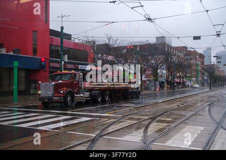 Regnerische Straßenansicht eines roten Lastwagens, der neben nassen Straßenbahnschienen und überhängenden Verkehrskabeln in Chinatown in der Nähe des Kensington Market in Toronto, Ontario, fährt Stockfoto