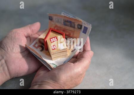 Ältere Hände, die Rechnungen und ein Miniaturhaus halten, Konzept für den Kauf oder Verkauf eines Hauses, Sparen, Versicherung, Spende für Obdachlose, Hypothek und r Stockfoto