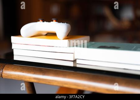 Weißer Google-Stadia-Controller, der auf einem Stapel Bücher auf einem hölzernen Couchtisch in einem gemütlichen Stockfoto