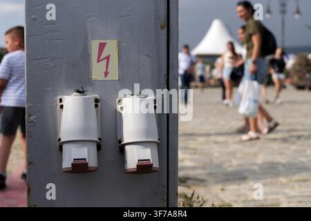 Öffentlicher Versorgungskasten mit zwei elektrischen Steckdosen und einem Hochspannungs-Warnschild. Verschwommene Menschen, die im Hintergrund laufen. Bulgarien, Varna, 8. Aug. Stockfoto