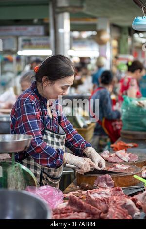 Fleischabteilung auf einem Straßenfoodmarkt in Vietnam, Verkäuferin schneidet frisches Fleisch auf dem Brett mit einem Messer. Stockfoto