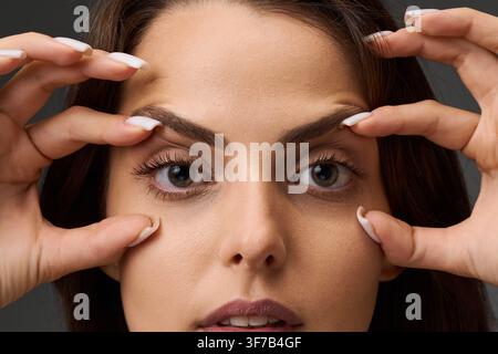 Nahaufnahme-Porträt einer Frau, die den Zustand ihrer oberen und unteren Augenlider zeigt, indem sie die Haut mit ihren Fingern berührt. Blepharoplastik und Augenli Stockfoto