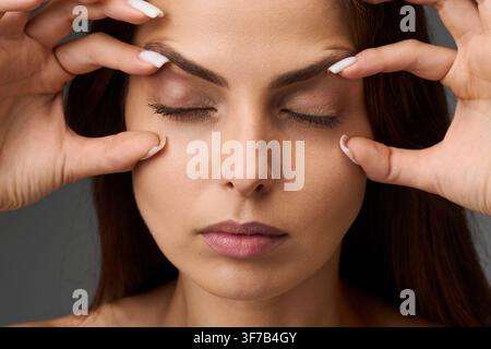 Nahaufnahme-Porträt einer Frau, die den Zustand ihrer oberen und unteren Augenlider zeigt, indem sie die Haut mit ihren Fingern berührt. Blepharoplastik und Augenli Stockfoto