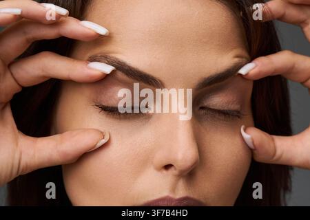 Frau, die den Zustand ihrer oberen und unteren Augenlider zeigt, indem sie die Haut mit den Fingern berührt, für das Konzept der Blepharoplastik und Augenlidkorrektur. Stockfoto