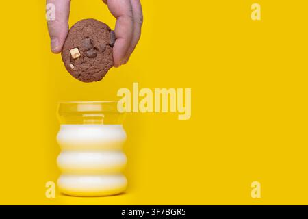 Schokoladenchip-Keks, der über einem Glas Milch auf einem gelben Studiohintergrund positioniert ist. Stockfoto