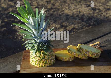 Frisch geschnittene Ananas und hellgelbe Scheiben, die auf einem Holzschneidebrett im Freien ruhen, betonen gesunde tropische Früchte Stockfoto