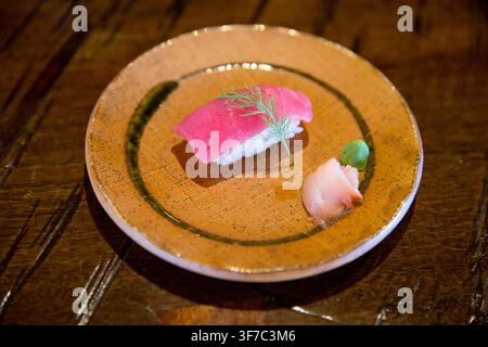 Eine hochwinklige Nahaufnahme eines Lifestyle-Food-Fotos, das ein einzelnes Stück frischen Thunfisch (Maguro)-Nigiri-Sushi zeigt, garniert mit einem zarten Dillzweig, Ser Stockfoto