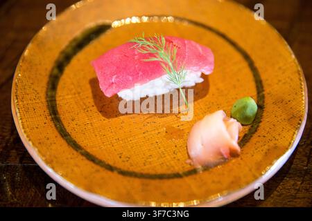 Eine hochwinklige Nahaufnahme eines Lifestyle-Food-Fotos, das ein einzelnes Stück frischen Thunfisch (Maguro)-Nigiri-Sushi zeigt, garniert mit einem zarten Dillzweig, Ser Stockfoto