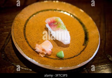 Eine hochwinklige Nahaufnahme eines Lebensmittelfotos, das ein einzelnes Stück frischen weißen Fisch-Nigiri-Sushi mit einer dunkelroten Blutlinie hervorhebt, garniert mit Stockfoto