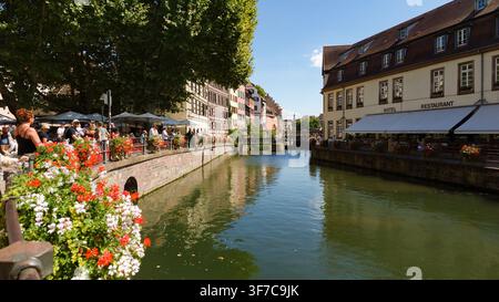STRASBOURG, FRANKREICH - 6. AUGUST 2026 - Strasbourg Petite France mit dem Fluss Ill, halb hölzernen Gebäuden und von Menschen gefüllten Restaurantterrassen Stockfoto