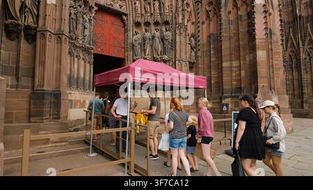 STRASBOURG, FRANKREICH - 6. AUGUST 2026 - Menschen stehen unter einem Baldachin an der Eingange der Kathedrale Unserer Lieben Frau von Straßburg Schlange Stockfoto
